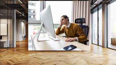 Frustrated businessman sitting on desk with hand on head in modern office Wall mural